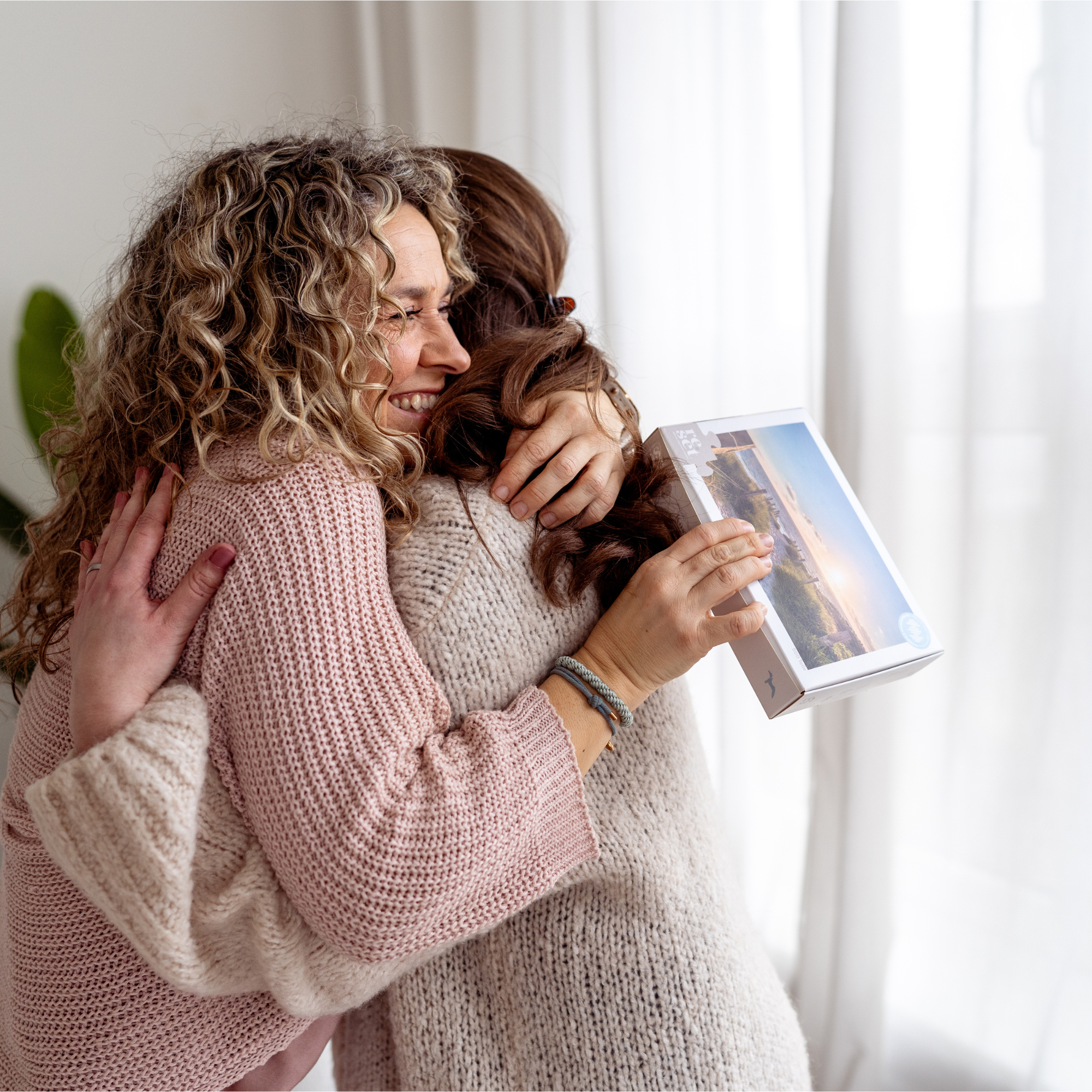 Zwei Frauen umarmen sich, eine hält eine Geschenkbox mit Landschaftsbild