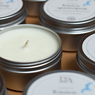 Mehrere weiße Duftkerzen in runden Metallbehältern mit Deckeln, eine Kerze ist geöffnet und sichtbar