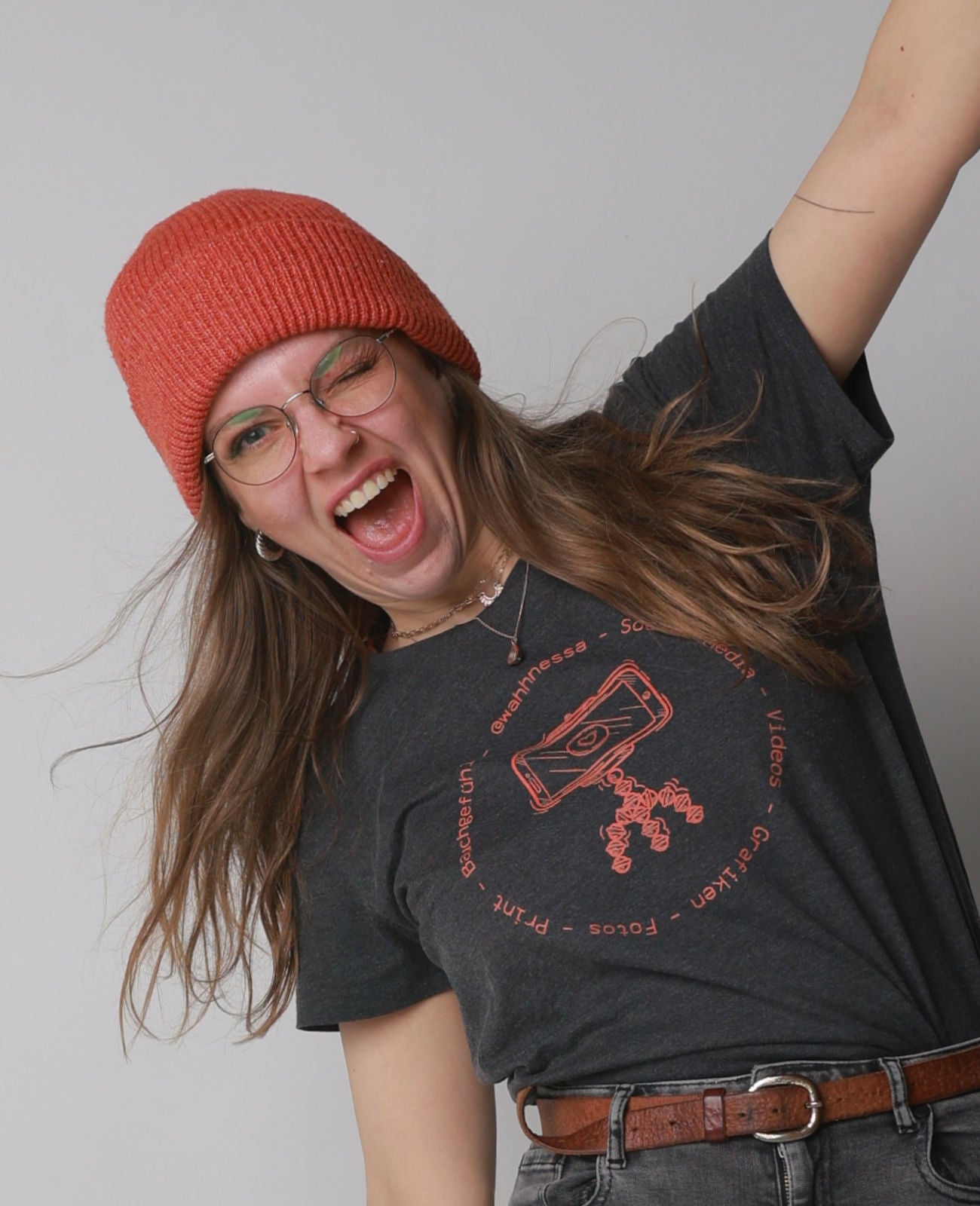 Person mit roter Strickmütze und schwarzem T-Shirt mit rotem Kassettenmotiv und Text, die einen Arm hebt