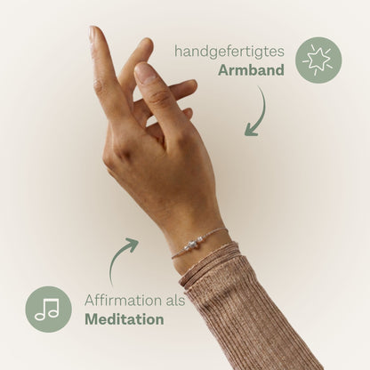 Hand mit hellbraunem Strickärmel trägt ein zartes Armband mit kleinen Perlen. Zwei grüne Kreise mit weißen Symbolen und Text heben das Armband sowie den Begriff Affirmation hervor. Der Text lautet: 'handgefertigtes Armband' und 'Affirmation als Meditation'. Pfeile verbinden die Kreise mit dem Armband und der Hand.